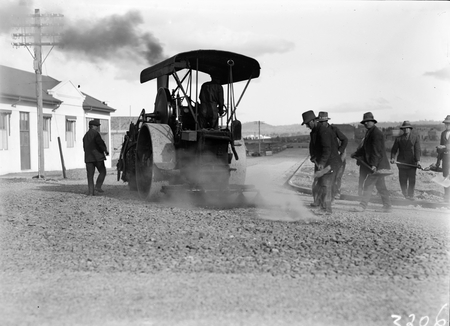 Mort Street, South from Canberra Times Office. Road making with steamroller spraying tar and workmen spreading road gravel.
