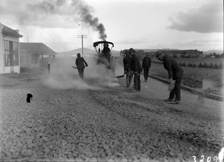 Road works in Mort Street, Canberra City with steamroller and workmen spreading gravel.
