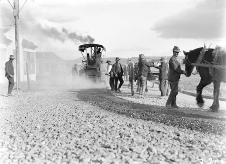 Steamroller spraying tar and workers spreading gravel from drays in Mort Street, Canberra City.