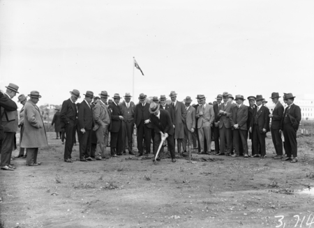 A crowd of onlookers with the Rt. Hon. Stanley Melbourne Bruce on shovel.