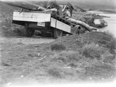 Motor truck carrying log about to cross a river.