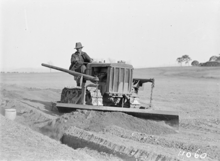 International crawler tractor with scraper attachment filling earth into a trench.