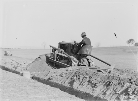 International crawler tractor with scraper attachment filling earth into a trench.
