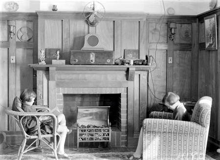 Sitting room with two girls reading, electric fire, wireless, wall lights and fan