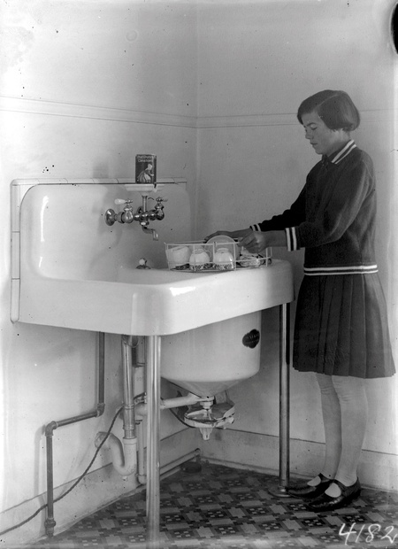 Girl at the kitchen sink loading crockery into a dish washer