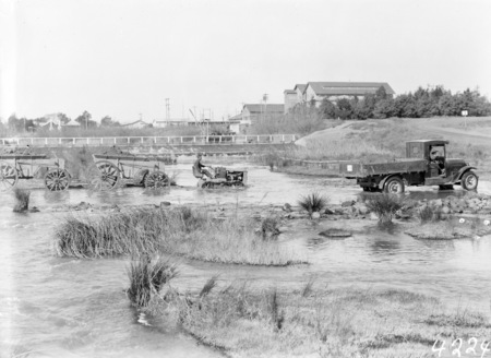 Cletrac Tractor towing wagons carrying river gravel in Molonglo River near the Kingston Power Station. Note Footbridge across the Power Station weir to Duntroon.
