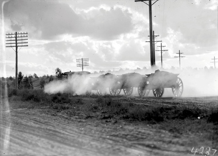 Tractor towing two loaded  wagons. Details obscured by dust