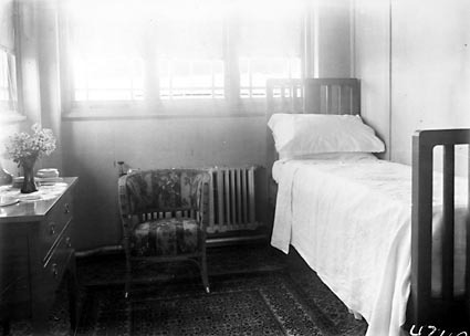 Dressing table,chair and bed in a bedroom.Steam radiator on back wall