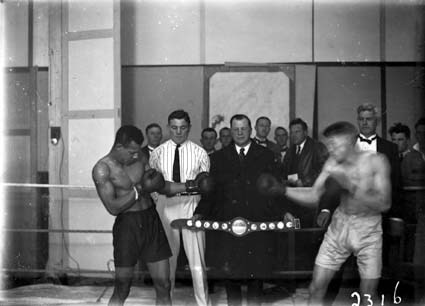 Two boxers with trophy belt and spectators.