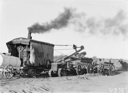 Keystone steam shovel loading wagons pulled by crawler tractor.