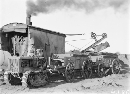 Keystone steam shovel loading wagons pulled by crawler tractor.