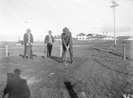 Three golfers at the tee, with the Hotel Canberra in background.