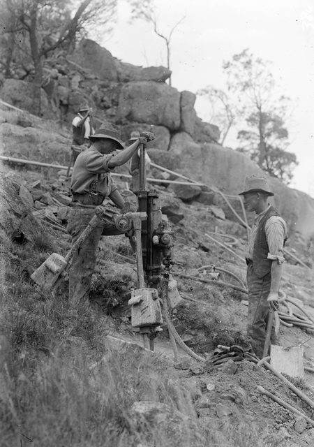 Quarrymen and compressed air drill preparing for blasting.
