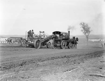Traction engine towing a road grader and wagons drawn by horses.