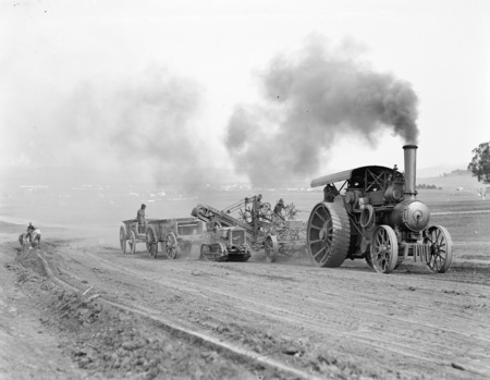 Traction engine towing a road grader loading a wagon hauled by a Cletrac crawler tractor.