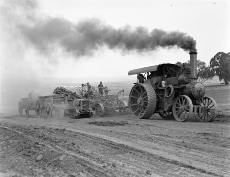 Traction engine towing a road grader loading a wagon and a Cletrac crawler tractor towing a wagon.