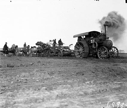Steam traction engine towing a ditch digger loading horse drays