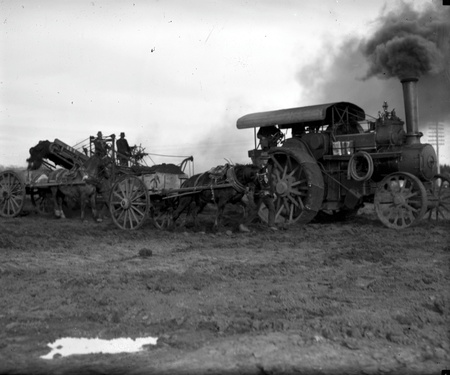 Steam traction engine towing a ditch digger loading horse drays
