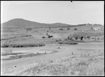 Crawler tractors and scoop excavating for a road and bridge at Scotts Crossing near the Molonglo River. Mount Ainslie on left, Russell Hill on right, Blundells cottage on right.
