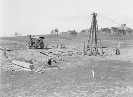 Steam traction engine operating pile driver for bridge construction.