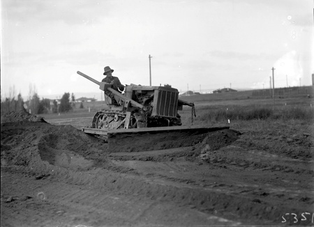 Crawler tractor with bulldozer attachment filling a drainage ditch