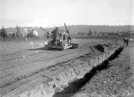 Crawler tractor with bulldozer attachment filling a drainage ditch