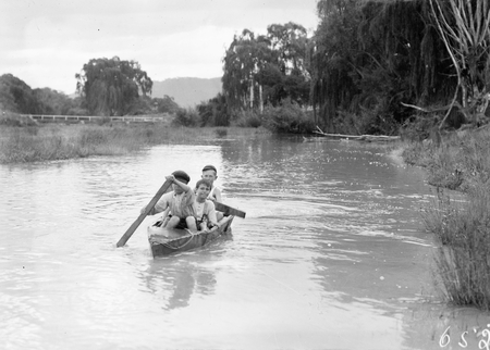 Three boys in a home made canoe on the Molonglo River. Note the palings for paddles.