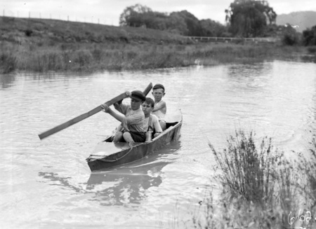 Three boys in a home made canoe on the Molonglo River. Note the palings for paddles.