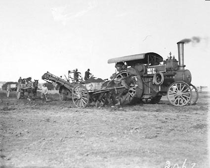 Steam traction engine towing a digger loading earth into horse drays