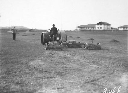Tractor towing multiple lawn mowers on Royal Canberra golf course - Canberra Hotel in background
