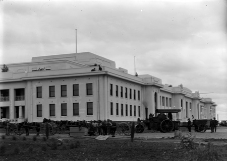 Steamroller towing two wheeled trailer with drays constructing roads outside Parliament House.