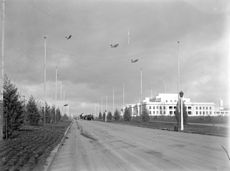 Royal Visit, May 1927. King George Terrace and Parliament House looking east showing flagpoles and young trees. RAAF flight overhead.