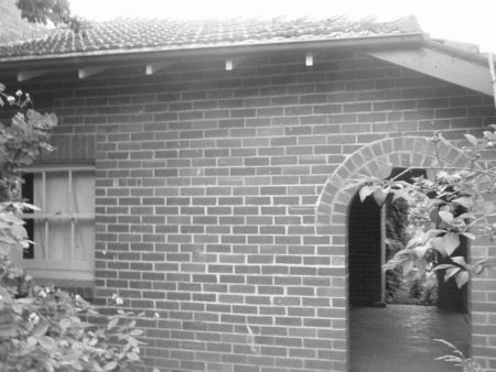 Evidence that this is a photo of Braddon, not Kingston: This is a closeup (in b&w) of the south wall of 65 Elimatta St.  With a bit of imagination you can see the  line of light coloured mortar on the left of the vertical part of the arch.  A high resolution copy of the original would help.  The fence running from the wall to the boundary fence no longer exists.  However, there are a couple of wooden pegs still in the wall of the house.  